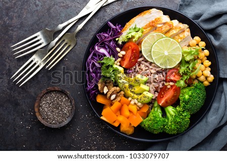 Buddha bowl dish with chicken fillet, brown rice, avocado, pepper, tomato, broccoli, red cabbage, chickpea, fresh lettuce salad, pine nuts and walnuts. Healthy balanced eating. Top view Royalty-Free Stock Photo #1033079707