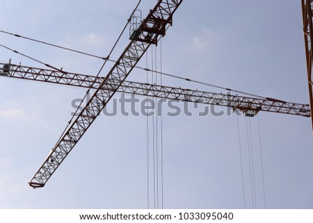 Close up outdoor view from below  of two cranes crossed arms. Silhouettes of the two technological elements with cables. Blue sky in background. Abstract industrial picture taken in a french city. 