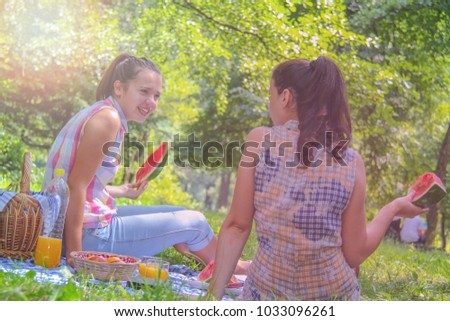Two young women enjoying  conversation and eating watermelon on picnic outdoors