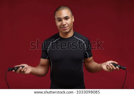 Picture of cool handsome young Afro American guy wearing dry fit black t-shirt exercising in gym using jumping rope, looking at camera with confident smile. Sports, fitness and jump-rope workout