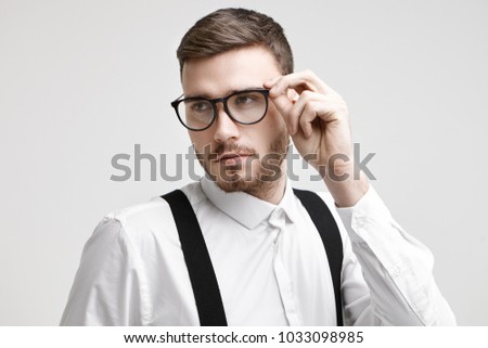 People, style, optics and eyewear concept. Horizontal picture of confident handsome young unshaven European male wearing white formal shirt with black suspenders, adjusting stylish spectacles