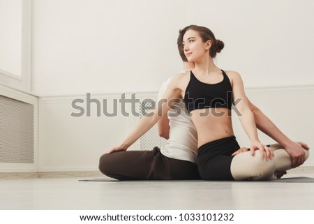 Young couple practicing yoga together. Man and woman sitting back to back on mat and twisting around partner, copy space. Partner yoga concept