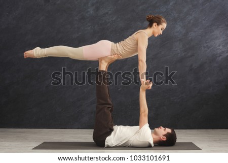 Young couple practicing acroyoga on mat in gym together. Man and woman doing yoga exercise, copy space, side view. Partner yoga, flexibility, balance and trust concept