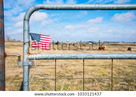 Small American Flag hanging on Metal Gate to open field and Country Ranch Home