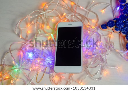 Mobile smart phone and led lights on a light wooden texture background. Festive decoration ornament with smartphone flat lay mock up telecommunication technology design