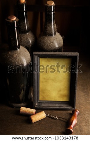 Still-life with old dusty wine bottles, corkscrew and blank picture frame