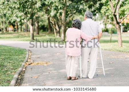 Back view of loving senior couple talking a walk with walker in the park Royalty-Free Stock Photo #1033145680
