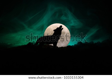 Silhouette of howling wolf against dark toned foggy background and full moon or Wolf in silhouette howling to the full moon. Halloween horror concept. Selective focus