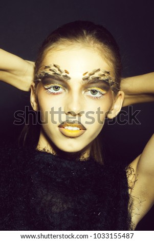 Closeup portrait of one beautiful wild young woman with bright golden animal monkey makeup with thorns on face in studio on black background, vertical picture