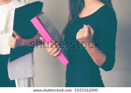 Yes. Young mature businesswomen holding file and graph date celebrating victory shouting happily with colleague in the office. Women holds fist as successful celebration winner emotion excitement.