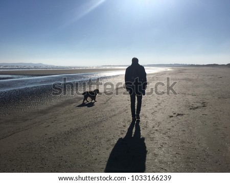 Man silhouette walking dog along beach in winter sun