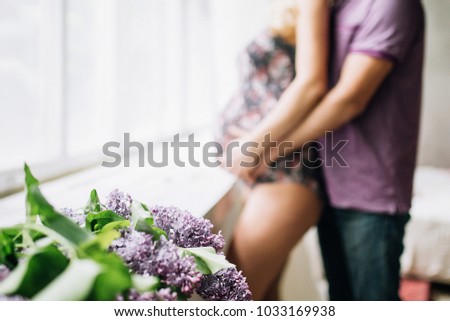 close-up of lilac flowers that lie on the window on the background of which stands a pregnant girl in the arms of a man