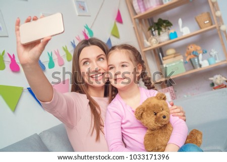 Mother and daughter together at home taking photos on smartphone