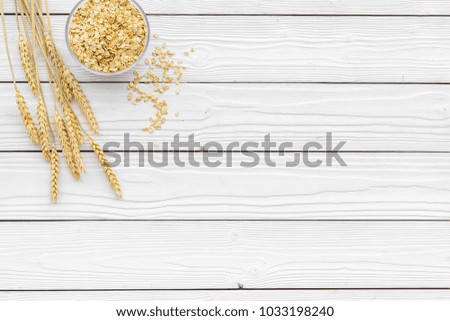 Cereals background. Raw oatmeal near sprigs of wheat on white wooden background top view copy space