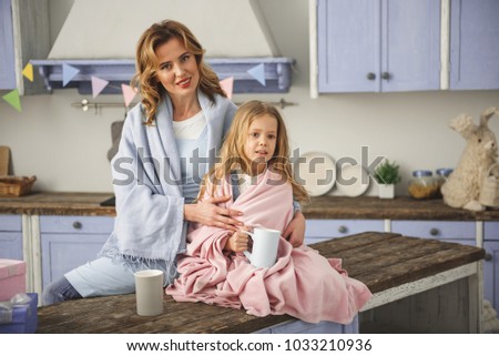 Portrait of calm family sitting on the dining table wrapped in blanket and holding cup of beverage. Copy space in right side