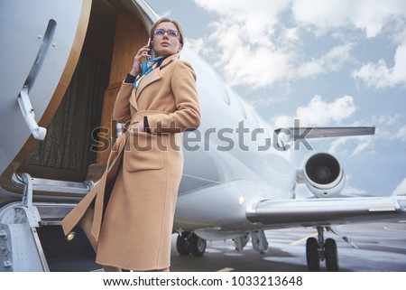 Low angle portrait of serene girl talking by phone while entering in aircraft. Career concept Royalty-Free Stock Photo #1033213648