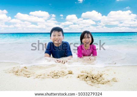 Picture of two little children looks happy while lying on the sand. Shot in the beach