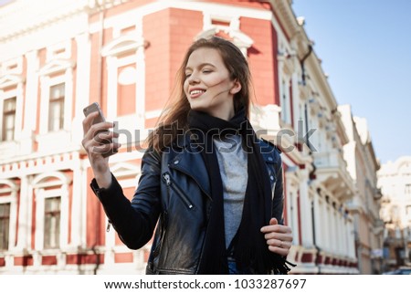 Time for selfie. Outdoor shot of attractive businesswoman on trip with company teammates, walking around city while having spare time, holding smartphone, wanting to take picture
