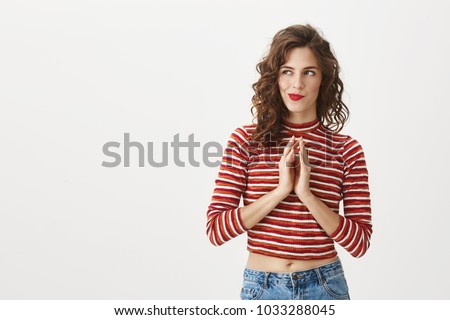 I have great idea. Studio shot of attractive female moving fingers near chest as if making up plan in mind, smiling mysteriously while looking aside, wanting to do something illegally or secretly Royalty-Free Stock Photo #1033288045
