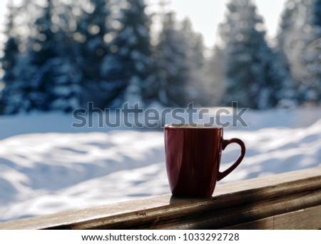 Red cup with hot drink and beautiful winter landscape with snowy firs. Winter relax time.