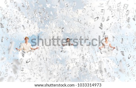 Young family keeping eyes closed and looking concentrated while meditating among flying letters in the air with cloudy skyscape on background.