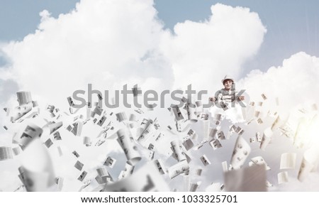 Young little boy keeping eyes closed and looking concentrated while meditating among flying papers in the air with cloudy skyscape on background.