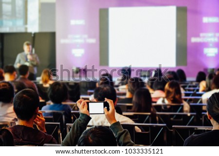 Audience using smart phone technology for take a photo and listening speaker who standing in front of the room at the conference hall, Business and Entrepreneurship concept.