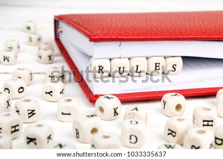 Word Rules written in wooden blocks in red notebook on white wooden table. Wooden abc.