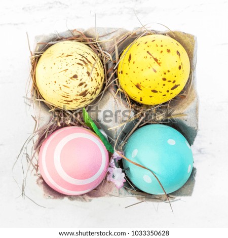 Easter eggs in egg cartoon box on white rustic wooden background close up. Festive decorations. Happy Easter!
