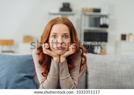 Portrait of young red-haired upset woman sitting on sofa at home Royalty-Free Stock Photo #1033351117