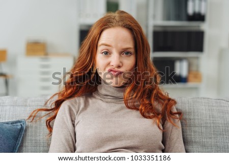 Pretty young redhead woman pulling a funny face making an exaggerated grimace with her lips as she sits on a sofa at home