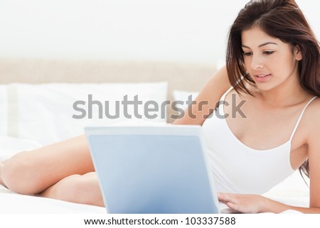 A woman using her laptop in front of her to browse while she lies on her bed.
