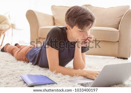 Tired teenager boy using laptop while doing homework indoors
