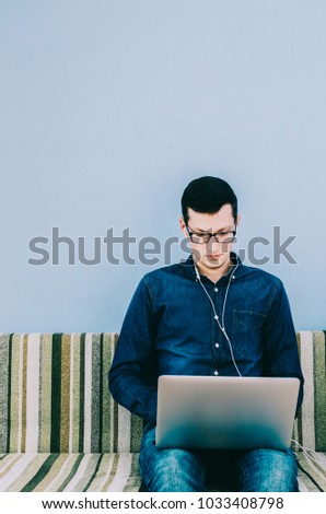 Young man with glasses sitting on sofa with laptop