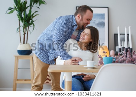 Picture of happy husband hugging pregnant wife sitting at table with candles