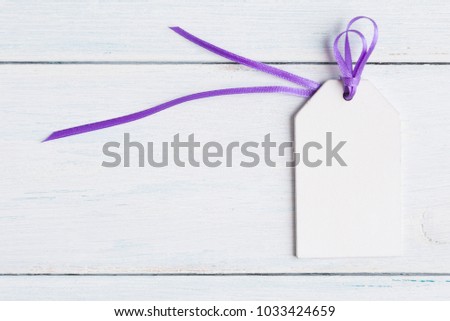 Blank tag with purple ribbon on white wooden background.