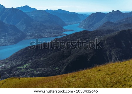 Panoramic View of beautiful landscape in the Italian Alps with fresh green meadows and snow-capped mountain tops in the background on a sunny day with blue sky and clouds in springtime.