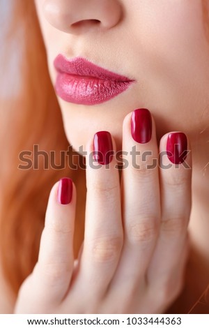 Beautiful red-haired young woman with red manicure, lipstick same color. Close up Portrait.