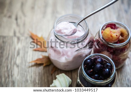 
pink yogurt in a glass jar and frozen currant berries and raspberries on a wooden background