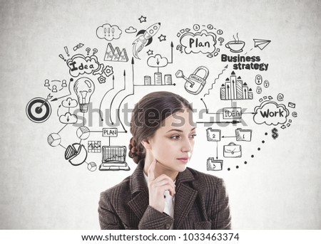 Thoughtful young woman with long dark hair wearing a suit is thinking. She is looking sideways and touching her face with a finger. A concrete wall with a business strategy sketch