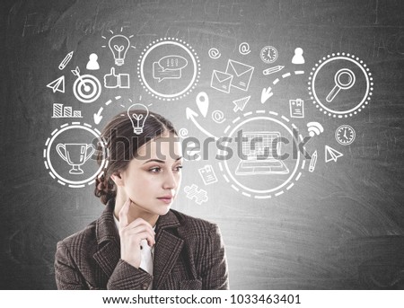Thoughtful young woman with long dark hair wearing a suit is thinking. She is looking sideways and touching her face with a finger. A blackboard with a plan to business success sketch