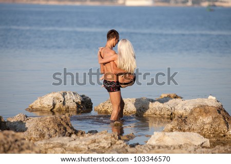 Attractive couple at the sea. Young man carrying blondie walking along wild rocky seashore