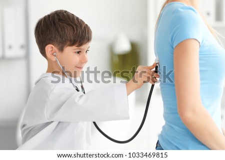 Cute little boy in doctor uniform examining patient indoors