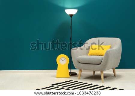 Trendy armchair with lamp near shaded spruce wall