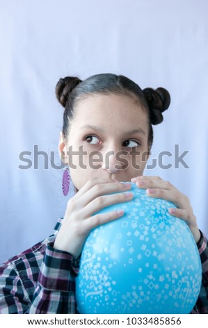 A teenage girl in a checkered shirt inflates an airy blue ball