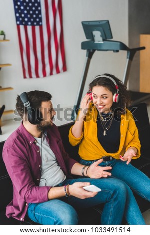 View of couple listening music in headphones and sitting on couch