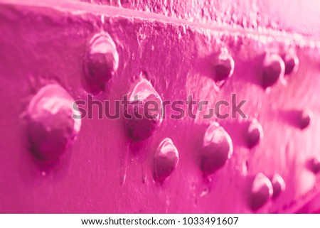Pink paint on metal rivets close up.