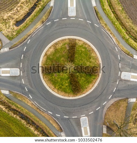 Aerial view of a small roundabout at the intersection of two asphalted gray country roads in the north of Germany, abstract