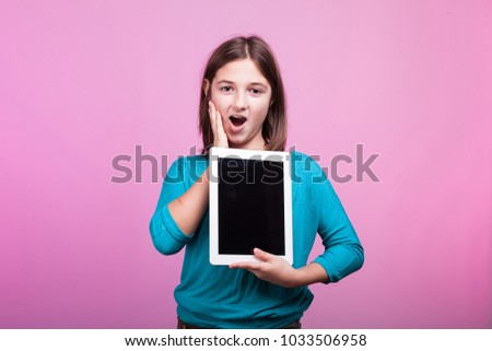 Beautiful young teenager girl with a digital tablet in her hands on pink background in studio photo