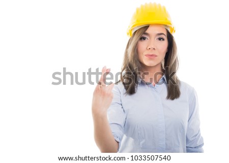 Portrait of female constructor holding fingers crossed on white background with copypsace advertising area